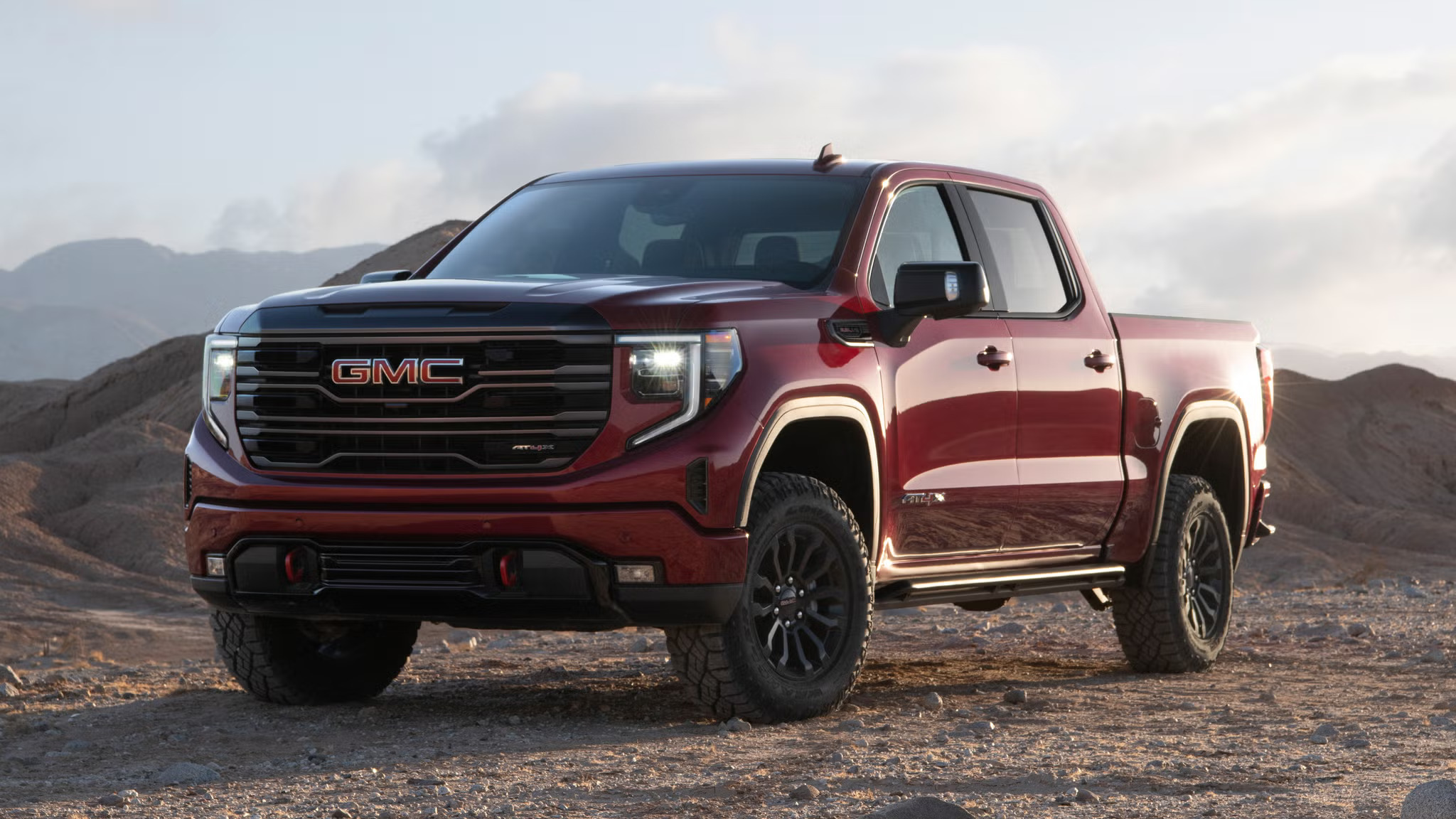A red GMC Sierra 1500 dominates the rugged terrain, set against a backdrop of endless desert and vivid blue skies